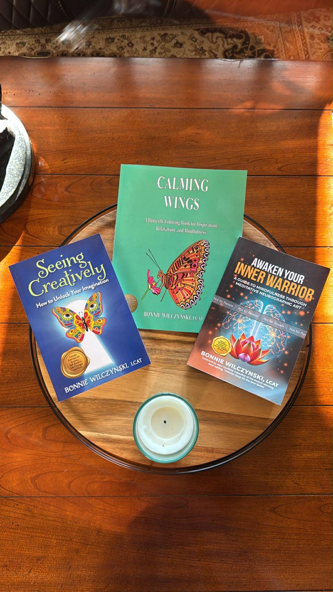 Three books and a candle arranged on a round wooden tray.